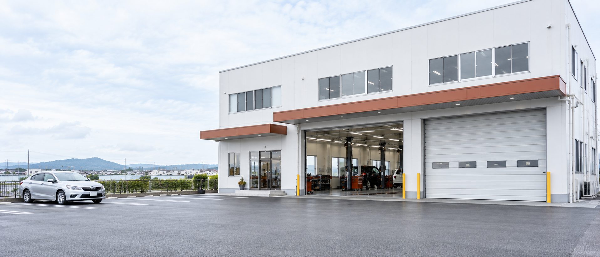 白い外壁の社屋と大きなシャッター開口が並ぶ工場の外観