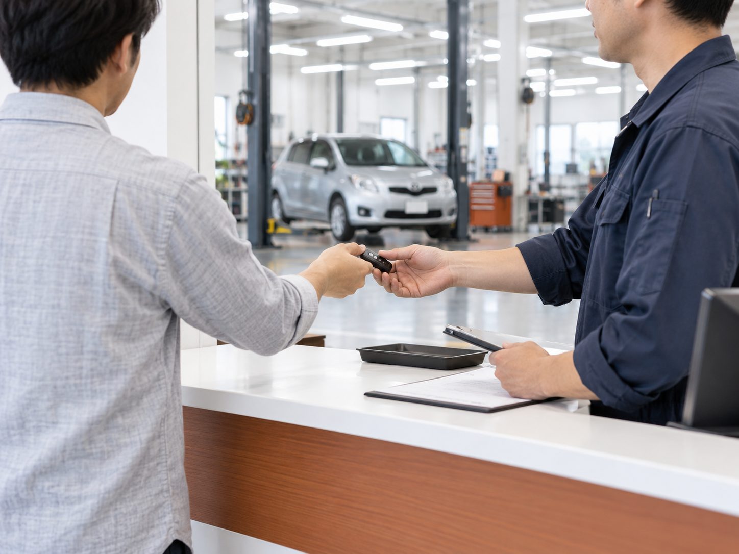 受付カウンターで来店したお客様から車のキーを預かる整備士